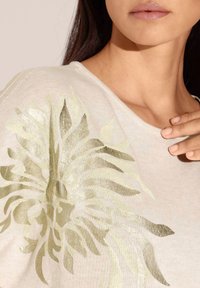 Lichtbeige trui met een metallic groene bloemenprint aan één kant, gebreide textuur en een brede halslijn. Gladde stof en een ontspannen pasvorm.