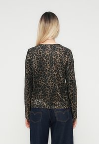 Žena s rovnými blond vlasmi, oblečená v čierno-hnedom topu s leopardím vzorom s dlhým rukávom a tmavomodrých džínsoch, zobrazená zozadu.