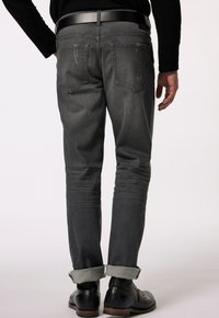 Jeans in denim grigio con vestibilità slim, caratterizzati da un orlo arrotolato, dettagli di whisker delicati e due tasche posteriori. Indossati con una cintura nera e stivali.