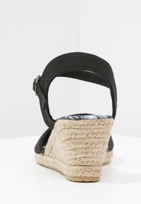 Černé látkové klínové sandály s řemínkem kolem kotníku a pleteným podpatkem pokrytým jutu zobrazené zezadu na bílém pozadí.