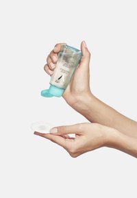 Clear plastic bottle with turquoise cap, holding a liquid. Hand dispensing product onto a white cotton pad. Smooth texture, modern design.