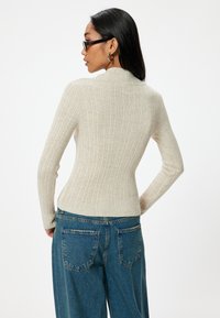 Lichtbeige geribde trui met een hoge hals en lange mouwen, gecombineerd met blauwe high-waisted jeans met achterzakken.