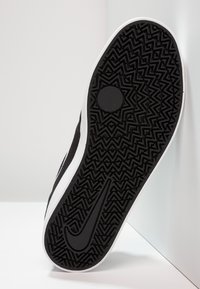 Mustmustel sneakeri taldil on struktureeritud, sakilise mustriga. Sellel on valge äär ja silmapaistev must Nike'i swoosh logo.