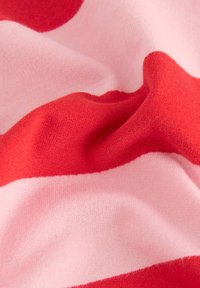 Tissu rayé rouge et rose avec une apparence douce et texturée. Le matériau présente de légers plis, mettant en valeur les couleurs contrastées.