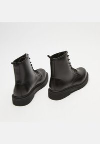 Stivali ankle in pelle nera con finitura liscia, punta rotonda, lacci frontali e suola in gomma testurizzata. Presenta dettagli di cucitura sui lati.