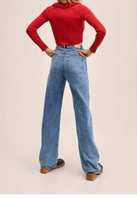 Maglietta a maniche lunghe rossa con coste abbinata a jeans blu chiaro a vita alta e zoccoli in legno scuro con tacco. Texture del denim liscia visibile.