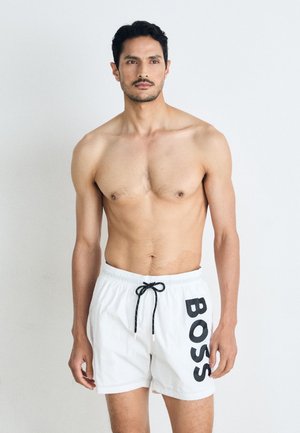 White swim shorts with black "BOSS" logo on the side, drawstring waistband, lightweight fabric, and relaxed fit. No other details visible.
