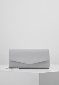Pochette rectangulaire grise avec fermeture à rabat et bandoulière en chaîne argentée reposant sur une surface blanche.