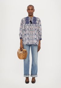 Fließende Bluse mit floralem Muster, dunkelblauem Kragen und Schleife; hellblaue Jeans; Handtasche aus Bambus; braune Schuhe mit Riemen.