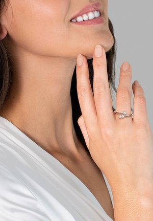 Silberring mit zwei klaren Steinen, zartes Design, glatte Textur und minimalistischer Stil, getragen an einer Hand mit natürlichen Nägeln.