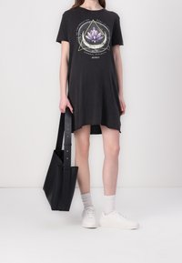 Robe en coton gris à manches courtes avec un design graphique représentant un lotus, des accents triangulaires et un ourlet asymétrique. Sac fourre-tout noir et baskets blanches inclus.