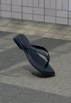 Mustad kaunistatud rihmadega plätu, mis ripub asfaldist kõnnitee kohal plaaditud seina ääres.