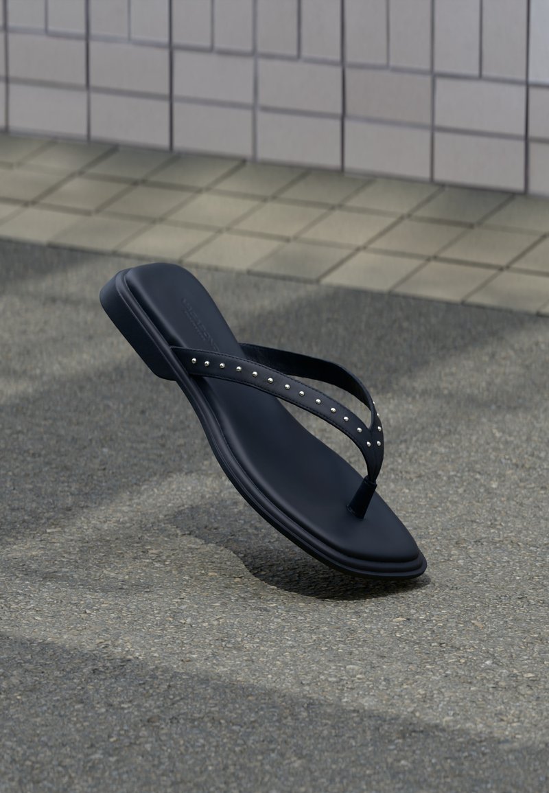 Μαύρο σανδάλι σαγιονάρας με τρουκς στα λουράκια, κρεμασμένο πάνω από άσφαλτο κοντά στην άκρη πλακιδωτού τοίχου.