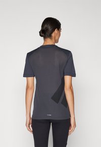 T-shirt de sport gris foncé en tissu maillé texturé, à manches courtes, avec des accents géométriques noirs contrastants au dos.