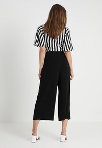 Černé široké kalhoty v kombinaci s černobílým pruhovaným krátkým rukávem, který má rozšířené rukávy a přiléhavý pas.