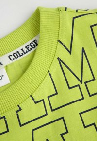 Zielony bawełniany sweter z prążkowanym kołnierzykiem i wyraźnym granatowym nadrukiem. Miękka tekstura i delikatny połysk, eksponujące sportowy styl.