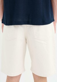 Shorts de mezclilla blanca con un corte relajado, que cuentan con dos bolsillos traseros. La tela parece resistente y tiene una textura suave. El dobladillo está terminado.