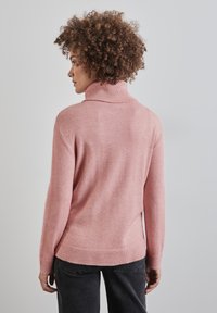 Suéter de cuello alto de color rosa claro con ribete en el cuello y los puños, textura suave, corte relajado y un dobladillo trasero ligeramente más largo.