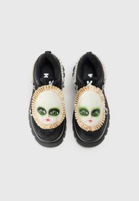 Scarpe platform nere con grandi volti di bambola che presentano ombretto verde e bordo arricciato beige sulla parte superiore, decorate con dettagli in perle.