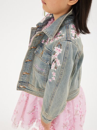 Giacca in denim con ricami floreali in rosa e bianco, caratterizzata da un colletto classico, chiusura frontale con bottoni e maniche lunghe.