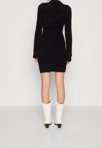 Czarna, teksturowana mini sukienka z długimi rękawami i wysokim kołnierzem, zestawiona z białymi kowbojkami z cienkim noskiem i masywnym obcasem.