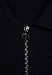 Mørkeblå zip-up skjorte med en tekstureret stof. Har en sølvfarvet metallynlås ned langs midten, fremhævet af en ren finish.