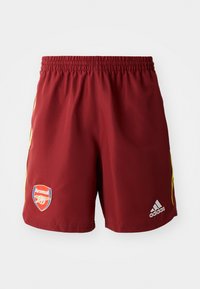 Røde sportsbukser med tekstur, elastisk talje, gule sidelister, Arsenal-logo nederst til venstre og Adidas-logo til højre.