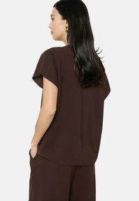 Top corto marrone a maniche corte con vestibilità rilassata, caratterizzato da un collo rotondo e una texture liscia. Abbinato a pantaloni marroni coordinati.