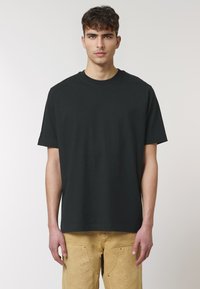 Zwarte katoenen t-shirt met korte mouwen, ronde hals en een relaxte pasvorm, gecombineerd met beige broeken met zakken en metalen accenten.