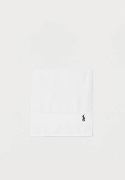 Toalla blanca doblada con un pequeño logo negro bordado de un jugador de polo a caballo en la esquina inferior derecha.