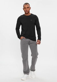 Svart langermet T-skjorte med rund hals, kombinert med grå jeans og hvite joggesko; har et lite merke på brystet.