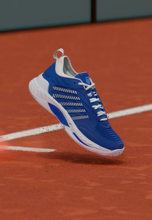 Sinine ja valge spordijalats hõljub punase saviselt tenniseväljakult, tõstes valgete piirjoonte lähedal üles savipuru.