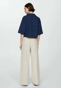 Navy cropped jacket with a collared neckline, short sleeves, paired with beige wide-leg trousers, featuring a smooth texture and relaxed fit.