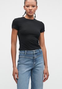 Czarna, dopasowana bluzka z krótkim rękawem w połączeniu z jasnoniebieskimi dżinsami z wysokim stanem. Bluzka ma gładką teksturę i prosty design, nie posiada wyraźnych detali.
