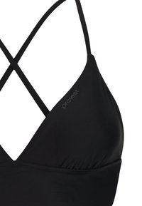 Zwarte bikinibovenstuk met dunne gekruiste bandjes en subtiel "protest"-logo op één cup tegen een witte achtergrond.