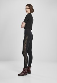 Svarte høytliv leggings med leopardmønster på sidepanelet, kombinert med en tettsittende svart kortermet topp og blanke røde snørebåndsko til ankelen.