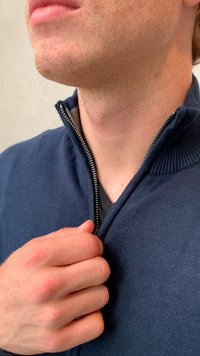Jūras zila rāvējslēdzēja džemperis ar ribotu apkakli, kuram ir metāla rāvējslēdzējs. Audums ir adīts, tam ir gluda struktūra un pieguloša forma.