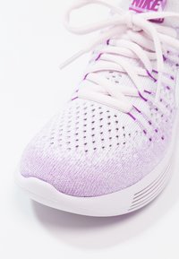 Zbliżenie białego i jasnofioletowego plecionego buta do biegania Nike z sznurówkami zawiązanymi na kokardkę i perforowaną, oddychającą cholewką.