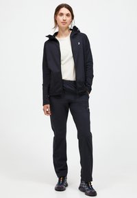 Black zip-up jacket with hood, paired with a light-colored shirt and dark pants. Features a simple design and lightweight material.