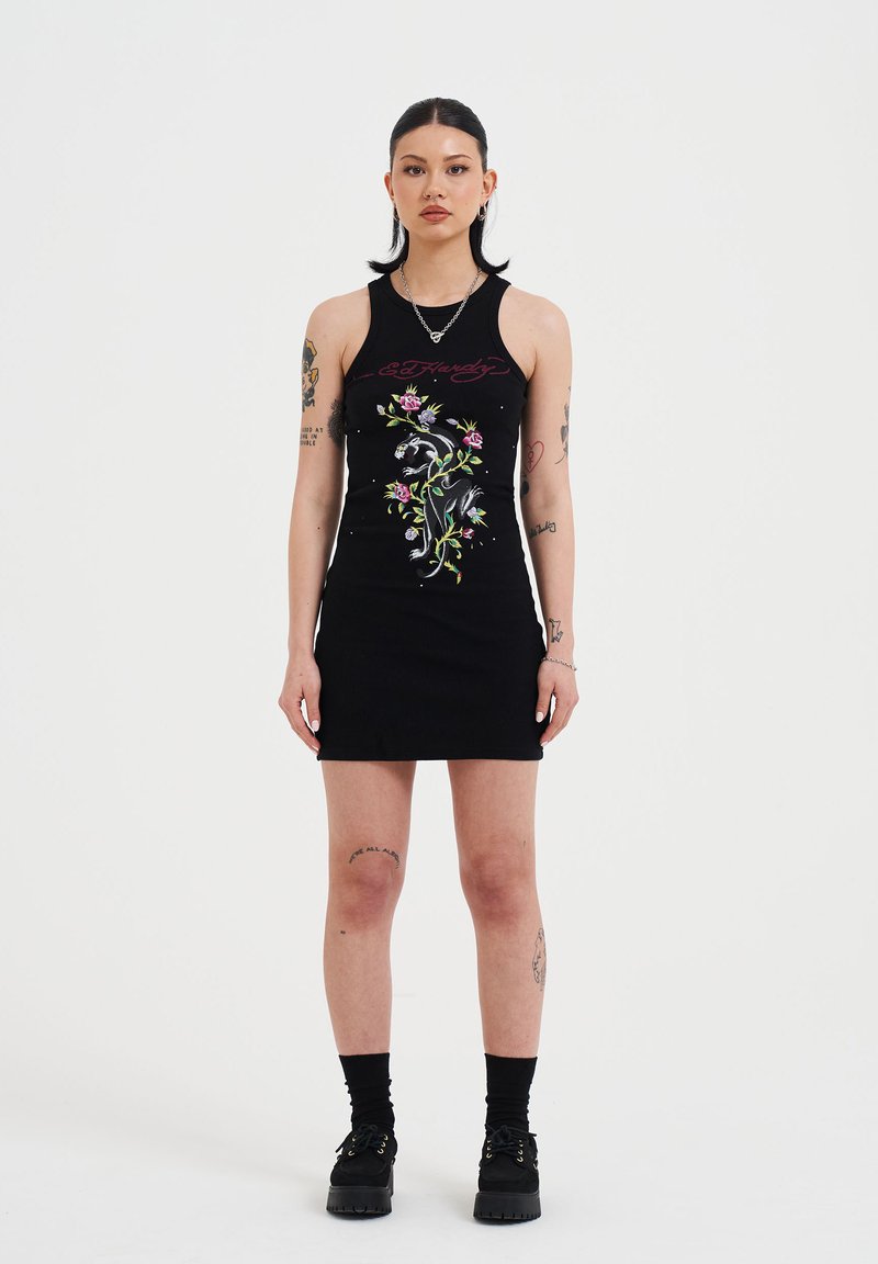Schwarzes ärmelloses Rippkleid mit buntem Blumenstickerei und Grafikdesign. Das Model trägt schwarze Plateauschuhe und Socken.