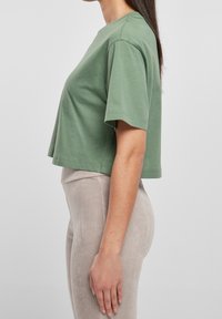 Olivově zelené zkrácené tričko s krátkým rukávem vyrobené z měkké bavlny. Má volný střih a čisté švy.