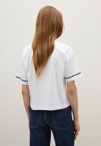 Witte t-shirt met korte mouwen en marineblauwe decoratieve stiksels langs de manchetten, met een ontspannen pasvorm en een cropped zoom.