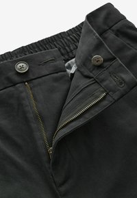 Schwarze Hose mit elastischem Bund, Reißverschluss und Knopfverschluss sowie Seitentaschen. Der Stoff hat eine glatte Textur mit einem dezenten Glanz.