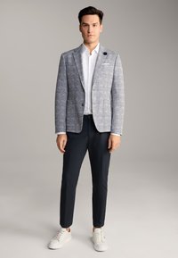 Blazer grigio chiaro a quadri con rever a punta, abbinato a una camicia bianca e pantaloni blu navy. Le sneakers bianche completano l'outfit. Tessuto liscio.