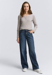 Ljusgrå långärmad henleytröja kombinerad med löst sittande blå jeans och vita sneakers, med knappslå och avslappnad passform.