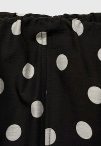 Țesătură neagră cu buline albe, cu textură adunată la guler și un detaliu cu fermoar vizibil pe cusătură.