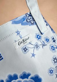 Blue floral-patterned tote made of durable fabric. Features a white interior, sturdy stitching, and a branded tag with "Cath Kidston London."