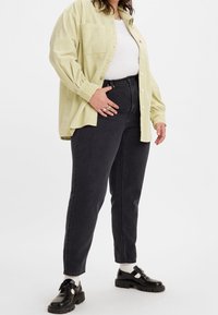 Světle zelená košile z manšestru s knoflíkovým zapínáním, doplněná černými džínami s vysokým pasem a černými botami s bílými ponožkami.