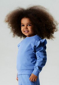 Sudadera azul claro con detalle de volantes en las mangas, hecha de tela suave, con cuello y puños acanalados, combinada con pantalones a juego.