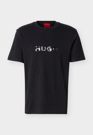 Svart kortermet T-skjorte med rund hals og skinnende sølvfarget "HUGO"-logo midt på brystet, samt en rød etikett på innsiden av kragen.